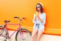 Fashion pretty woman drinks fruit juice from cup with retro bicycle over colorful orange