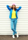 Fashion pretty woman model in colorful clothes posing over white background wearing pink hat yellow sunglasses and blue jacket Royalty Free Stock Photo