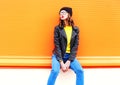 Fashion pretty woman model posing in black hat rock jacket over colorful orange background Royalty Free Stock Photo