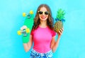 Fashion pretty woman with skateboard and pineapple sunglasses having fun over colorful blue