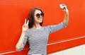 Fashion pretty woman wear a sunglasses and striped dress makes self-portrait on smartphone over red Royalty Free Stock Photo