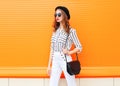 Fashion pretty woman wearing a black hat sunglasses white pants and handbag clutch over colorful orange Royalty Free Stock Photo