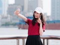 Fashion pretty young girl with black long hair, wearing red T-shirt and white baseball cap selfie with scissors hand pose outdoor