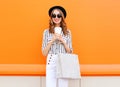 Fashion pretty young smiling woman model with shopping bag holding coffee cup wearing black hat white pants over colorful orange Royalty Free Stock Photo