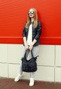 Fashion pretty young woman wearing a rock black leather jacket, sunglasses and bag over red Royalty Free Stock Photo