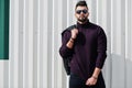 Fashion rich beard Arab man wear on turtle neck and sunglasses posed against green and white steel wall with jacket on hand.