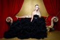 Fashion shoot of beautiful blond woman in a long black dress sitting on sofa Royalty Free Stock Photo