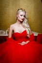 Fashion shoot of beautiful blond woman in a long black dress sitting on sofa Royalty Free Stock Photo