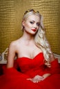 Fashion shoot of beautiful blond woman in a long red dress sitting on sof Royalty Free Stock Photo