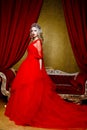 Fashion shoot of beautiful blond woman in a long red dress on vintage red sofa background Royalty Free Stock Photo