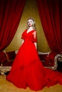 Fashion shoot of beautiful blond woman in a long red dress on vintage red sofa background Royalty Free Stock Photo