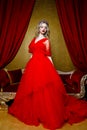 Fashion shoot of beautiful blond woman in a long red dress on vintage red sofa background Royalty Free Stock Photo