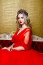 Fashion shoot of beautiful blond woman in a long red dress on vintage red sofa background Royalty Free Stock Photo