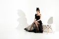 Fashion shot of elegant sad woman in black dress and veil sits on chair and waiting on white background Royalty Free Stock Photo