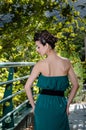 Fashion slim woman wearing green dress standing against bridge