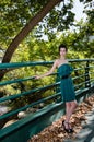 Fashion slim woman wearing green dress standing against bridge