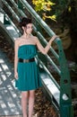 Fashion slim woman wearing green dress standing against bridge