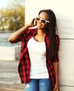 Fashion smiling african woman talking on a smartphone in the city, wearing a red checkered shirt sunglasses Royalty Free Stock Photo