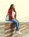 Fashion smiling african woman wearing a red checkered shirt and backpack resting in the city Royalty Free Stock Photo