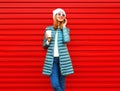 Fashion smiling woman talks on a smartphone holds coffee cup on red