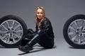 Fashion, sport, extreme. Smiling biker girl wearing motorcycle gear sitting on a floor with car wheels in a studio.