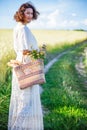 woman in white dress with basket with bread and milk walking along the trail in the field