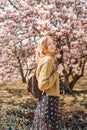 Beautiful 30s woman with long blonde hair posing between pink magnolia. Stunning girl looking at you or in camera. Royalty Free Stock Photo