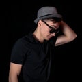 Fashion style portrait of muscular, young handsome man in black t-shirt with stylish hat and modern sunglasses