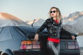 Fashion style wide angle young stylish attractive girl with bright red lips in a leather jacket and sunglasses stands