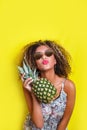 Fashion summer portrait afro american girl in sunglasses and pineapple over yellow background