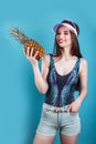 Fashion summer portrait beautiful woman in sun pink visor and pineapple over blue background Royalty Free Stock Photo