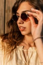 Fashion summer portrait of stylish pretty woman with curly hair put on a sunglasses near wooden wall at sunset Royalty Free Stock Photo