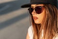 Fashion swag young girl with pretty lips in tender skin in stylish black baseball cap and trendy sunglasses on street at amazing Royalty Free Stock Photo