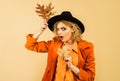 Fashion trend for fall. Beautiful surprised girl in orange stylish shirt, coat and black hat. Autumn woman in fedora hat