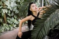 Fashion tropical portrait. Young attractive Asian woman model in trendy black overalls, with ponytail hair, sitting near Royalty Free Stock Photo