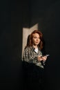 Fashion vertical portrait of beautiful young woman holding using mobile phone at shadow background in dark living room Royalty Free Stock Photo