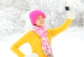 Fashion winter happy smiling young woman taking picture self portrait on smartphone over snowy trees wearing colorful knitted hat Royalty Free Stock Photo