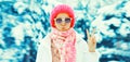 Fashion winter portrait of stylish young woman wearing sunglasses, colorful knitted hat and scarf in the park on snowy background Royalty Free Stock Photo