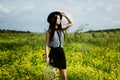 Fashion woman in black hat standing on yellow sunny flowers field