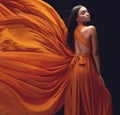 Fashion, woman and elegant, dress flying and style, beauty on dark background, portrait and model in orange in studio Royalty Free Stock Photo