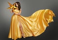 Fashion Woman in Golden Silk Dress with Big Gold Star. Beautiful Model in Yellow floating Gown over Gray background. Beauty Girl Royalty Free Stock Photo