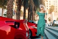 Fashion woman in green dress walk Dubai city streets. stands next to luxury sport cars. Arab Emirates travel