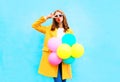 Fashion woman holds an air balloons in a yellow coat on colorful