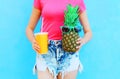 Fashion woman holds in hands cup of juice and pineapple with sunglasses over colorful Royalty Free Stock Photo