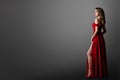 Fashion Woman in Long Red Dress. Model Showing Leg in Evening Silk Slit Gown. Side Profile View. Black Background with Copy Space