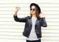 Fashion woman makes self portrait on smartphone in black rock style over white