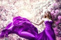 Fashion Woman Pink Dress in Spring Flower Garden. Beauty Model Girl in Purple Silk Gown Fluttering on Wind. Floral Pink Fantasy Royalty Free Stock Photo