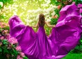 Fashion Woman in Purple Silk Dress Rear View in Spring Blossom Park. Elegant Model in Pink Satin Gown flying on Wind looking at