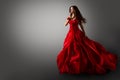 Fashion Woman in Red Dress. Beauty Model dancing in Long Evening Gown fluttering on Wind Black Hair flying in Air over Gray