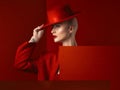 Fashion, woman and red hat with cosmetic or luxury in studio red background with creative retro suit. Style, runway and